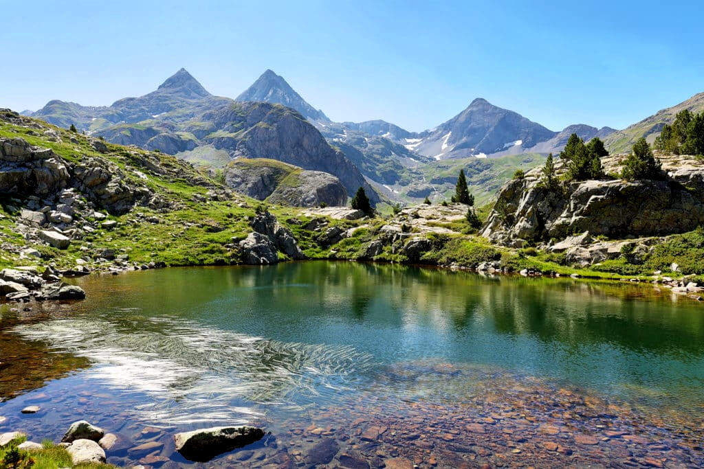 Lago de alta montaña en Aragón, rodeado de picos nevados y praderas verdes, perfecto para escenas de naturaleza.